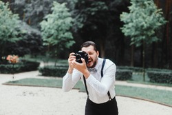 Young handsome beard man in white shirt and trousers makes beautiful pictures on film retro camera, stylishly dressed, photographer,outdoor portrait, close up,brutal, tattoo, street photo,photographer