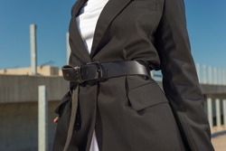 close-up details of a female business black jacket, on a waist a leather belt on an African fashion model, against a blue sky. Style, design of women's clothing. Black fashion girl