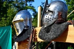 A close up on three well maintained medieval helmets with neck protection chainmail laying on a wooden table next to a cloth tent seen during a historic fair in Poland on a sunny summer day