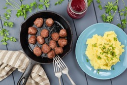 Sweden meatballs in cast iron pan, mashed potatoed with leek and berry sauce in glass jar served on gray wooden table