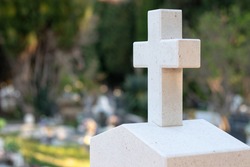 White stone cross with green orange marks worn over time marking a tombstone in a graveyard