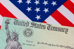 United States Treasury check and American flag. Concept of stimulus payment, tax refund and federal government grants, loans, benefits and assistance