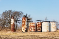 Old oil well storage tanks in farm field. Oil well abandonment, environment pollution, and oil production concept