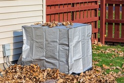 House air conditioning unit with protective cover during fall season. Concept of home air conditioning, hvac, repair, service, winterize and maintenance.