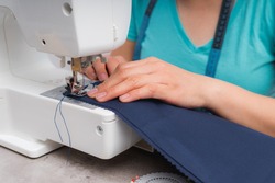 Cheerful woman sewing while sitting at her working place in fashion workshop