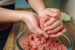 Close-up of a woman's hands preparing ground beef to make hamburgers, the meat is still raw and she is adding the ingredients, nice atmosphere in the kitchen.