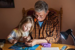 Grandfather shows coins to a small beautiful granddaughter through a magnifier. The concept of common interests and family unity. Family values.
