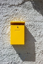 Yellow mailbox on the wall at sunny day. Box for letters and correspondence, vertical orientation