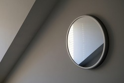 Round wall mirror reflections in a light grey room with angled dormer cornice. Sylish elegant and sophisticated. Simple enigmatic monochrome minimalist abstract interior design element. 