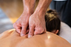 A young woman getting a relaxing natural massage in a cozy home environment. Close-up view of masseur hands giving massage therapy