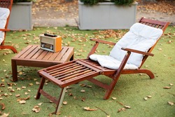 Wooden chair in autumn garden. Vintage radio on table. Wooden deckchair on green summer lawn on picnic. Lounge sunbed. Wooden garden furniture on grass lawn outdoor for relax. Backyard exterior. 