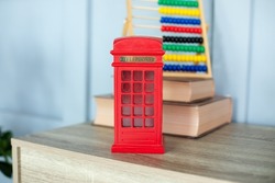 Figurine of a red telephone booth on shelf. Mini figurine of London Telephone Booth for sale as souvenir. Telephone booth present. Red british phone booth statuette decoration room. 
