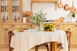 Stylish dining room with wooden table and chairs. Cozy cuisine  decorated with summer decor and  table setting summer flowers and fruits. Holiday family dinner. kitchen interior with utensils, pans