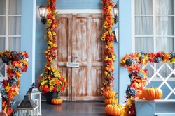 Halloween design home with yellow fall leaves and lanterns. House entrance staircase decorated for autumn holidays, fall flowers and pumpkins. Cozy wooden porch of the house with pumpkins in fall time