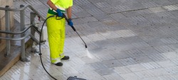 Worker cleaning a street sidewalk with high pressure water jet. Urban maintenance concept. Copy space