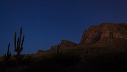 Nighttime Sonoran Desert landscape with saguaro cactus, Pleiades and other stars visible in the night sky above the foothills of the Catalina Mountains and Pusch Ridge in Oro Valley, Arizona. 