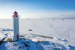 Lighthouse on winter island. Sea frozen fairway with ships in the background.