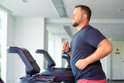chubby man walking on running track, warming up on gym treadmill