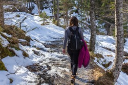Young woman walks in the Gaube Valley frozen path surrounded by rocky slope, spruce and pine trees, near Cauterets in the Haute-Pyrénées department, France.