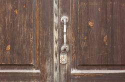 Old wooden entrance door with a metal handle. A dilapidated, antique door with an iron handle.