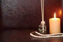 Aroma sticks, candle and string of pearls on a dark background
