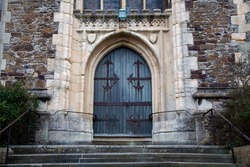 A wooden entrance door to a 15th century stone church set within a carved stone arch with steps leading up