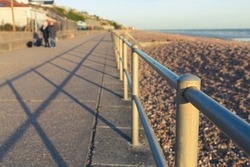 Abstract perspective looking down a seafront promenade with narrow depth of field fused on the railing with a couple waling their dogs blurred in the background