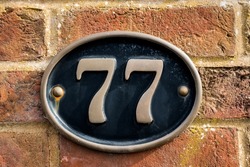 Residential house number 77 gold letters on a black metal plate on a red brick wall