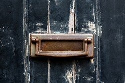 Weathered brass letterbox with knocker in an antique black painted door with peeling paint