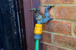 Garden hose attached to a metal tap in an exterior red brick wall