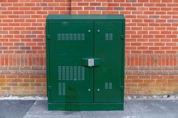 New fibre to premises local telecommunications street cabinet in dark green metal against a red brick wall