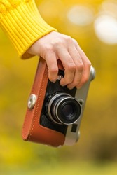 Woman hand with vintage retro photo camera outdoors in autumn day on yellow blurry background. Natural fall, defocused, bokeh background. Shallow depth of field