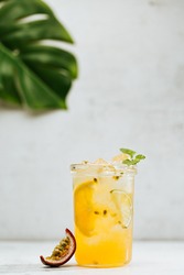 Lemonade or tropical cocktail with lemon, passion fruit, orange and mint, cold refreshing drink or beverage with ice on white table.
