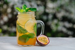 Lemonade or tropical cocktail with lemon, passion fruit, orange and mint, cold refreshing drink or beverage with ice on white table.
