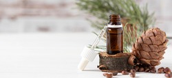 glass bottle with oil, pipette and cedar cone on light wooden background