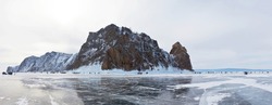 Frozen Lake Baikal. Groups of tourists arrive by car across the ice of the lake to Cape Hoboy, the tip of Olkhon Island. View from the ice to the famous Deva Rock. Winter travel. Natural background