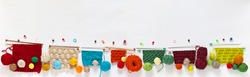 Panoramic top view on composition with knitting accessories: balls of colorful wool yarn, knitting needles and samples of different types of knitting on white background. Banner, copy space, flat lay