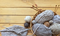 Handmade circular knitting with five needles, balls of woolen yarn and knitting needles on wooden background. Skeins of different types of beige and brown yarn in wicker basket. DIY concept