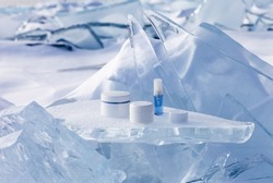 Cosmetic products for face and hand skin care in winter time. Advertising of nourishing cosmetics for cold weather on a podium stand from piece of ice against the backdrop of a frozen and snowy lake
