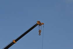 Hooks with steel crane slings and arms painted in yellow and black on a blue sky background. Used for lifting large objects or items weighing up to 25 tons.