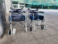Two blue wheelchairs are lined up in front of hospitals or shopping malls to serve the elderly, the sick or the handicapped. The trolley is made of steel with a dark blue seat and large black wheels.
