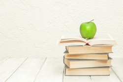 Stack of books with an open book and green apple on white wooden boards. Education background