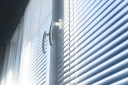 Light from the sun enters through the window blinds. Closed office blinds on the windows. Horizontal metal window blind.