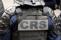 Close-up 'CRS' (riot police) marking written on the back of a tactical vest worn by a police officer on a street of Paris, France. Concepts of law and order, security and 
repression of hooliganism