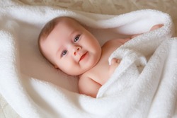 baby   is wearing diapers and a white towel in  bedroom. A newborn baby is resting in bed after a bath or shower. Children's room. Textiles and bedding for children.