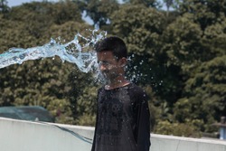 Head shot of teen boy getting splashed of water. Portrait of boy while facing the burst of water. Water splash on boy face