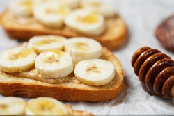 Delicious toasted sandwich bread with peanut butter, banana, honey on concrete background. Healthy, balanced traditional American school breakfast. Copy space, top view. Vegan sweet dessert