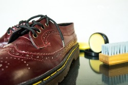 Maroon wingtip brogue made of genuine leather side by side with brush and shoe polish on white background