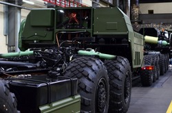 Heavy duty truck for transport missile defence system and non-standard cargo. Industrial workshop for the production of military trucks, wheel chassis and vehicles. Wheeled tractor background