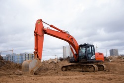Red excavator during earthmoving at construction site. Backhoe dig ground for the construction of foundation and laying sewer pipes district heating. Earth-moving heavy equipment on road works